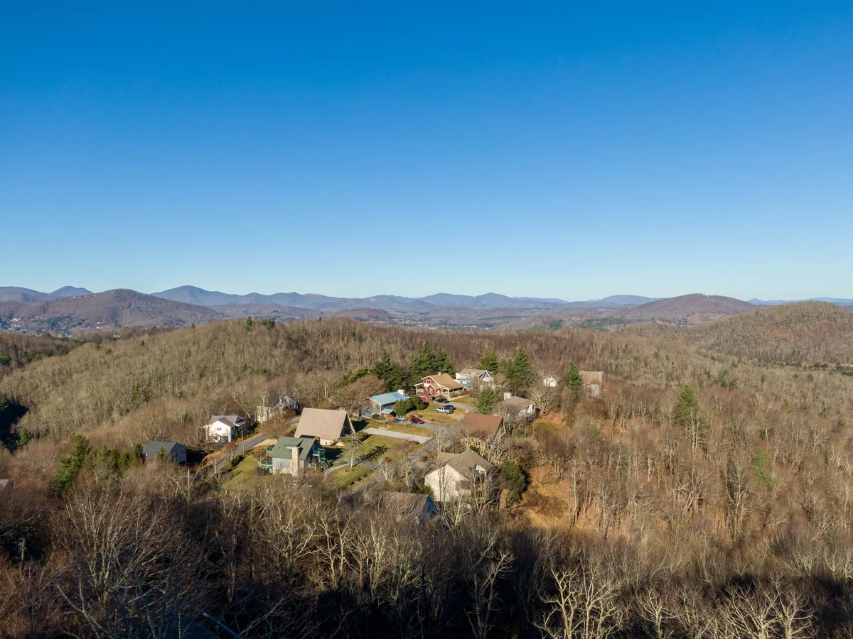 A sweeping view of the mountain range with a residential area nestled amid scattered trees, evoking the sense of adventure and natural beauty right at your doorstep. The scene suggests hiking, autumn foliage, community events, and access to scenic mountain landscapes.