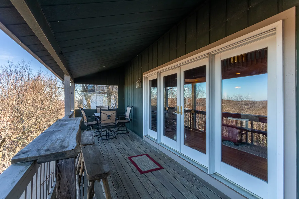 The covered deck off the main living area invites with comfortable outdoor seating, glass doors, and a natural wood railing overlooking distant mountain vistas. Morning sunlight bathes the space, making it ideal for sipping coffee at the bar or enjoying evening mountain breezes.