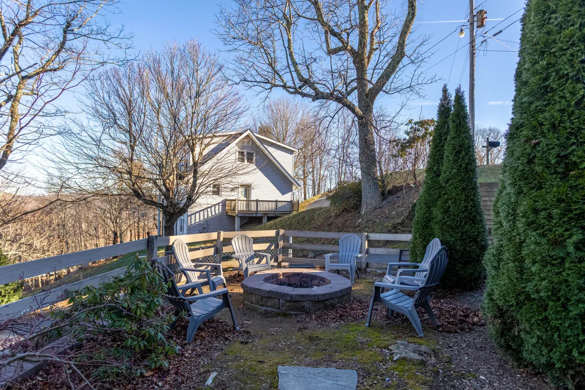 A cozy outdoor fire pit area framed by comfortable seating and surrounded by mature trees, perfect for gathering under the stars. The scene hints at stargazing, summer barbecues, and the glow of a crackling fire, reinforcing the lodge’s role in outdoor recreation and relaxation.