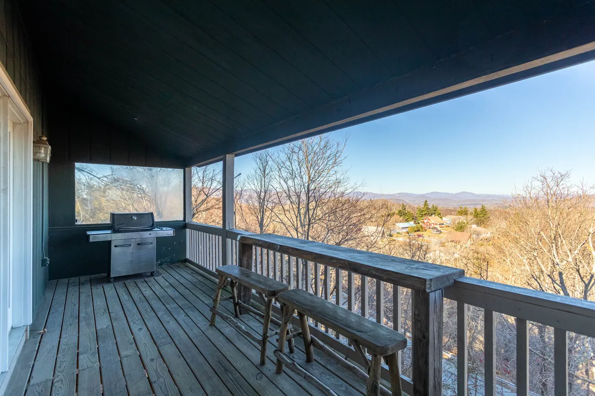 The covered deck features a grill, wooden railing, and sweeping mountain views, creating a picturesque setting for outdoor dining and summer barbecues.