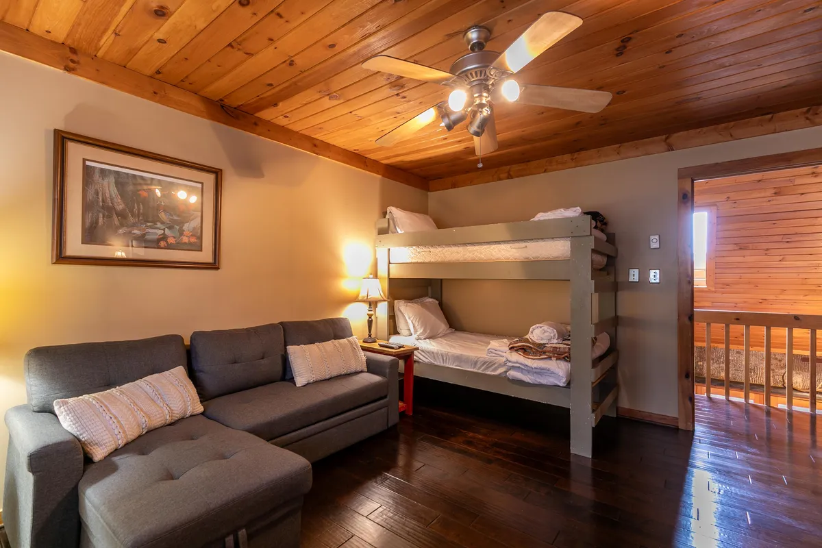 This image highlights a flexible bedroom/den setup with bunk beds, a sofa, a table lamp, and framed artwork. The arrangement is ideal for families or groups needing flexible sleeping options, with inviting decor that appeals to both kids and adults.