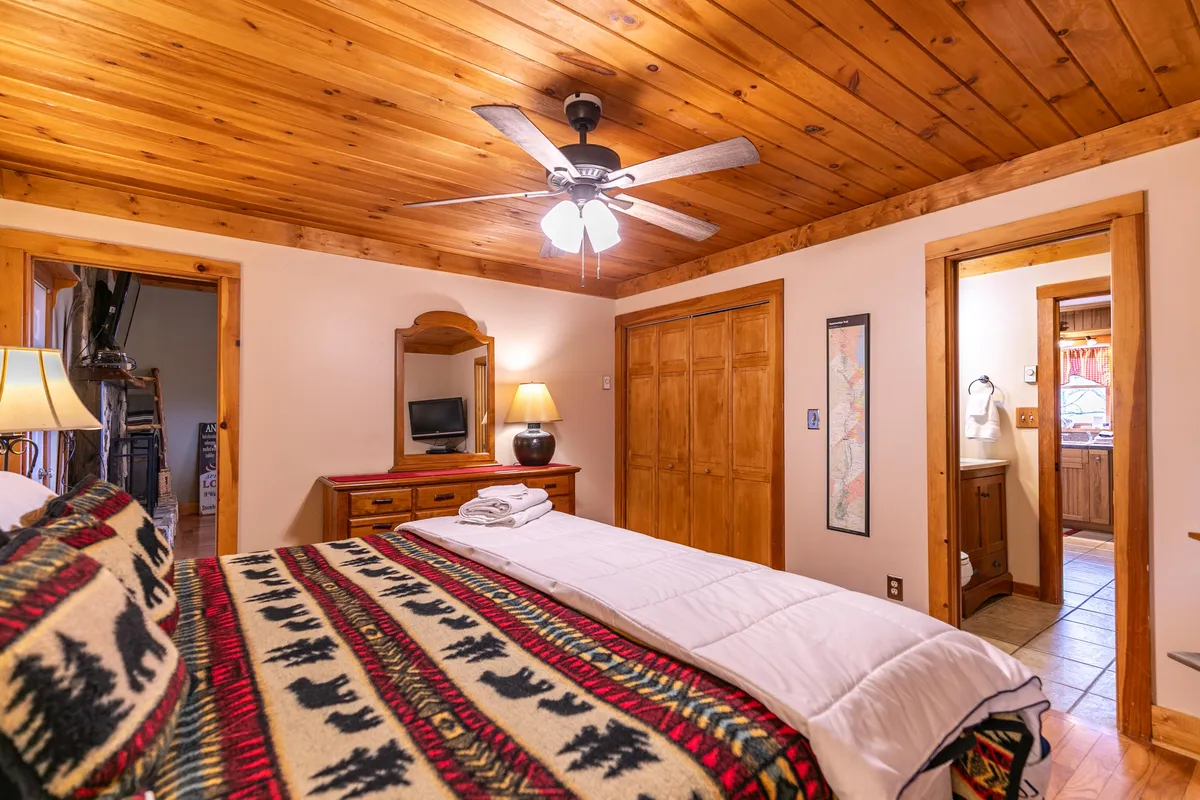 A tranquil bedroom with a patterned blanket on the bed, wooden ceiling, side table with a lamp, and a mirror. The space feels intimate, inviting couples to relax and enjoy a peaceful retreat.
