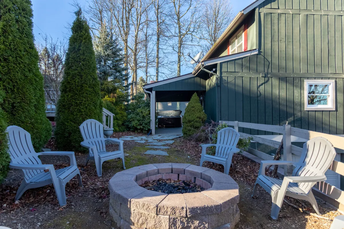 This cozy exterior scene centers on a fire pit encircled by Adirondack chairs, set within inviting landscaping. The setup encourages social gatherings, storytelling, and s’mores, with the soft glow of the fire creating a welcoming atmosphere for evenings under the stars.